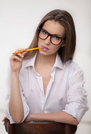Smart and beautiful. Thoughtful young woman holding pencil near mouth and looking at camera while sitting on the chairの写真素材