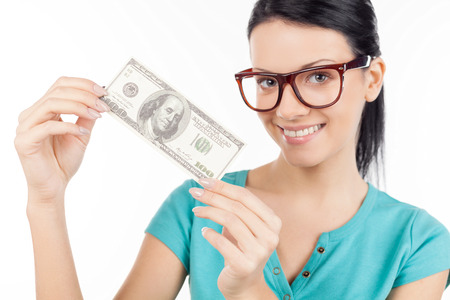 Rich and beautiful. Cheerful young woman in glasses holding one hundred dollar bill in her hands and smiling while standing isolated on whiteの写真素材