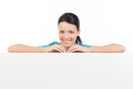 Leaning at copy space. Beautiful young woman leaning at copy space and smiling while standing isolated on whiteの写真素材