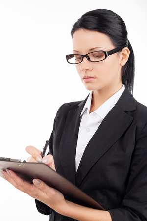 Confident businesswoman. Confident young business woman writing something in her note pad while standing isolated on whiteの写真素材