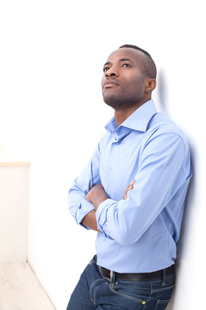 Thoughtful man. Handsome young black man keeping his arms crossed and looking up while leaning at the wallの写真素材
