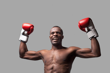 I am the best! Young African boxer raising his hands up and grimacing while standing isolated on...