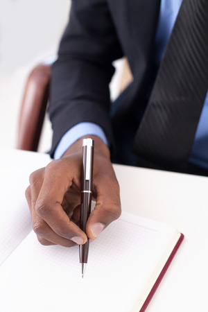 Making notes. Close-up of African businessman writing something in his note padの写真素材