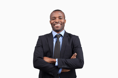 Confident businessman. Cheerful young African man in formalwear keeping arms crossed and smiling at camera while standing against white backgroundの写真素材
