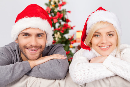 Celebrating Christmas together. Cheerful young couple sitting on the couch and smiling at cameraの写真素材