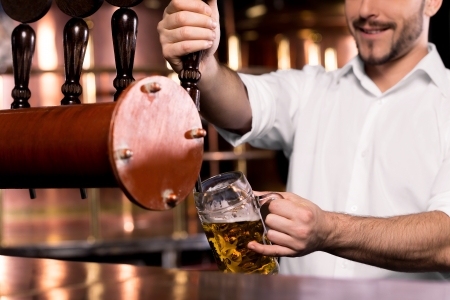 Pouring beer. Cropped image of smiley bartender poring beer to the mugの写真素材