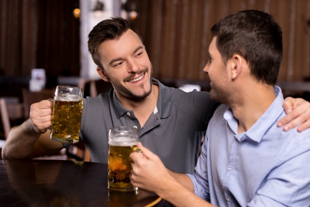 Relaxing in beer pub. Two cheerful young men drinking beer in barの写真素材