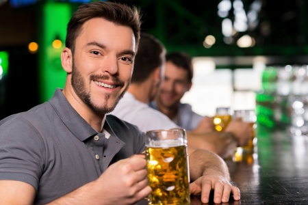 Man in bar. Handsome young man drinking beer in bar and smilingの写真素材