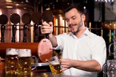 Freshly tapped beer. Cheerful young bartender pouring beer and smilingの写真素材