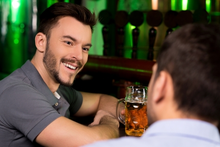 Spending time in bar. Two cheerful men talking to each while drinking beer in barの写真素材