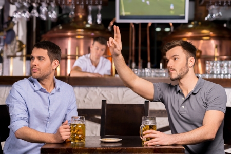 Waiter! Two young men sitting in bar while one of them calling a waiterの写真素材
