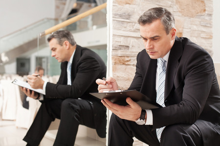 Businessman making notes. Confident mature man in formalwear making notes in his note pad while sitting on staircase の写真素材