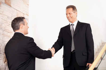 Handshake. Two business men in formalwear handshaking on staircase and smilingの写真素材