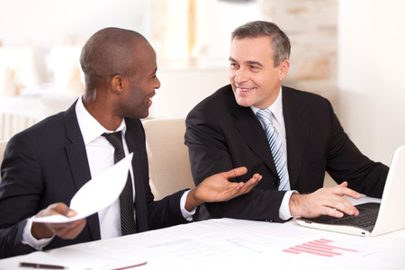 Discussing a project. Two cheerful business people in formalwear discussing something while one of them gesturing and smilingの写真素材