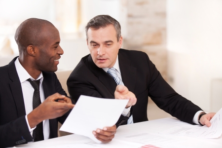 Contract on good conditions. Two cheerful business people in formalwear discussing something and pointing a paperの写真素材