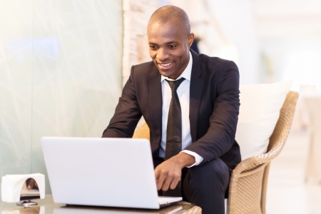 Business on the go. Cheerful young African businessman using his laptop while sitting at the restaurant の写真素材