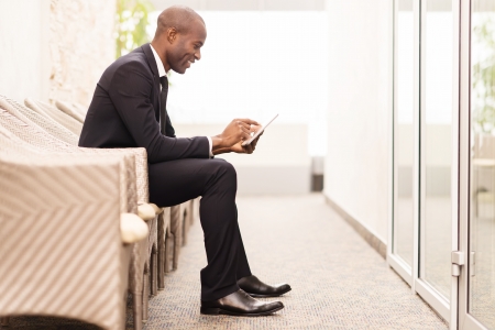 Checking his schedule on the go. Side view of cheerful young African businessman working on digital tablet while sitting on the chair の写真素材