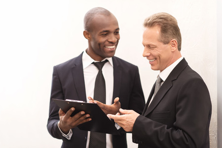 Discussing a new project. Two cheerful business men looking at the note pad and gesturingの写真素材