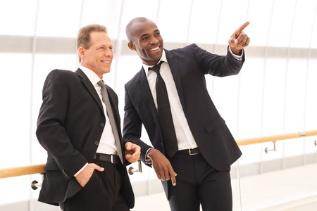 Business people. Two cheerful business men standing close to each other while one of them pointing away and smilingの写真素材