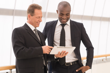 Discussing a new project. Two cheerful business men looking at the digital tablet and smilingの写真素材