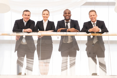 Business team. Low angle view of four confident business people standing close to each other and smiling at cameraの写真素材