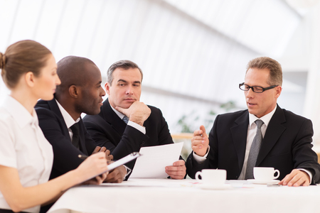 Business meeting. Business people in formalwear discussing something while sitting together at the tableの写真素材