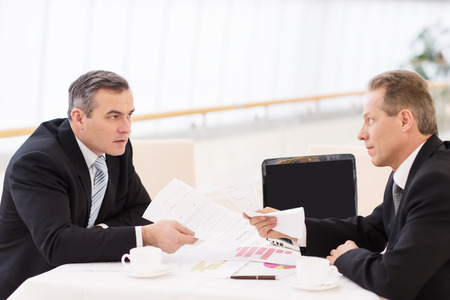 Business confrontation. Two mature men in formalwear arguing while sitting together at the tableの写真素材