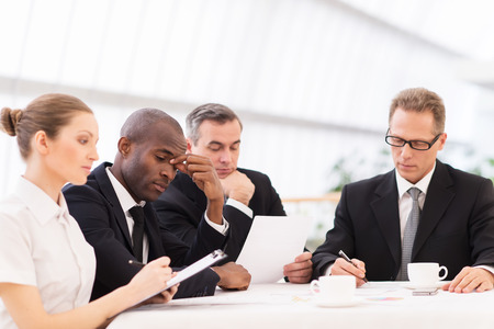 Tired business people. Four business people in formalwear looking tired while sitting together at the tableの写真素材