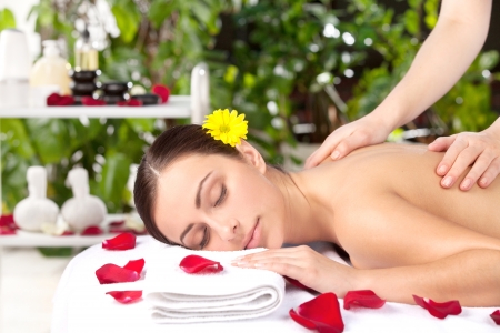 Spa girl. Beautiful young woman with flower in head lying on front while massage therapist massaging her backの写真素材