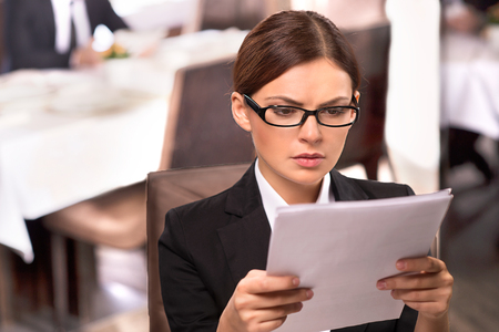 Stuck in paperwork. Thoughtful young woman in formalwear examining a document while sitting at the restaurantの写真素材