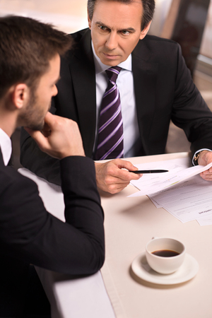 Business meeting at the restaurant. Top view of two business people in formalwear discussing something while one of them pointing paper with penの写真素材