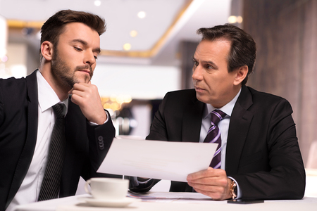Discussing contract. Two business people in formalwear discussing something while one of them showing a paper to another oneの写真素材