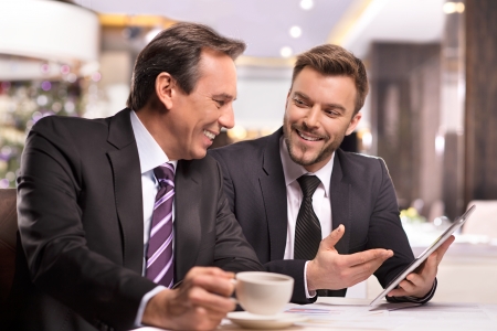 Successful project. Two cheerful business people in formalwear discussing something and smiling while one of them pointing digital tabletの写真素材
