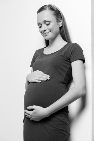 Pregnant woman. Black and white image of beautiful young pregnant woman touching her abdomen and looking at it with smileの写真素材