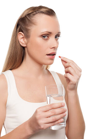 Woman taking pills. Depressed young woman taking a pill while standing isolated on white の写真素材