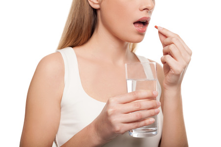 Woman taking pills. Depressed young woman taking a pill while standing isolated on white の写真素材