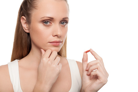 Woman with pill. Thoughtful young woman holding a pill and looking at cameraの写真素材