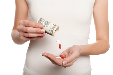 Paid medicine. Cropped image of woman pouring pills from the dollar bills while standing isolated on whiteの写真素材