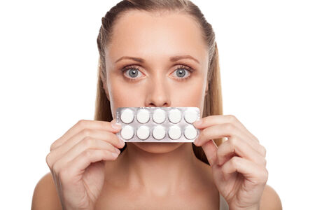 Woman with medicines. Shocked young woman holding pack of pills in front of her mouth while standing isolated on white の写真素材
