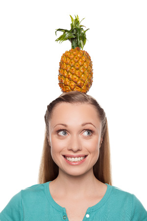 Pineapple on her head. Beautiful young woman holding pineapple on her head and smiling while isolated on whiteの写真素材