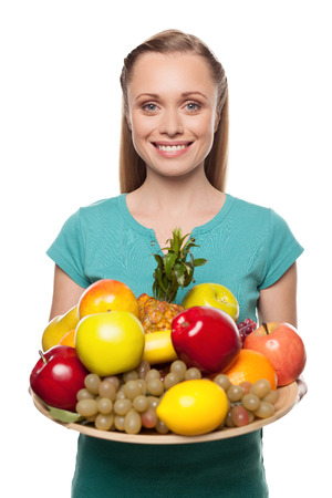 Woman with fruits. Beautiful young woman holding a plate with fruits and smiling while standing isolated on whiteの写真素材