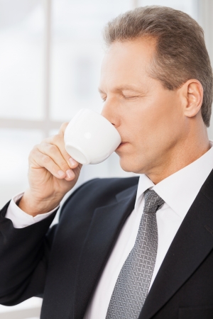 Morning coffee. Side view of mature man in formalwear drinking coffee and keeping eyes closed の写真素材