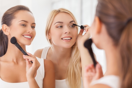 Doing make-up together. Two beautiful young women doing make-up together while looking at the mirror and smilingの写真素材