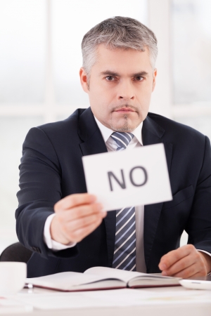 I said no! Serious senior man in formalwear holding a paper with no sign on it while sitting at her working placeの写真素材