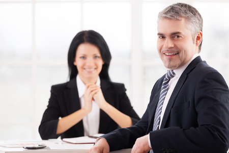 I got this job. Cheerful mature man in formal wear smiling at camera while woman in suit sittingの写真素材