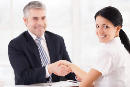 Good deal. Two people in formalwear handshaking and looking at camera while sitting at the tableの写真素材