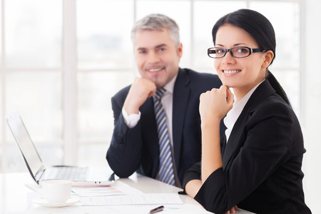 Business colleagues. Two cheerful business people smiling at camera while sitting at the table togetherの写真素材