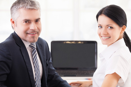 Working together. Cheerful man and woman in formalwear working on laptop and looking over shoulderの写真素材
