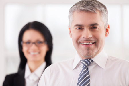 Cheerful business people. Confident mature man in shirt and tie looking at camera while woman in formal wear standing の写真素材