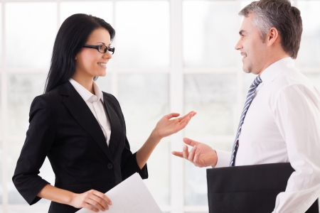Business colleagues discussing work. Two cheerful business people discussing something and gesturing while standing face to face の写真素材